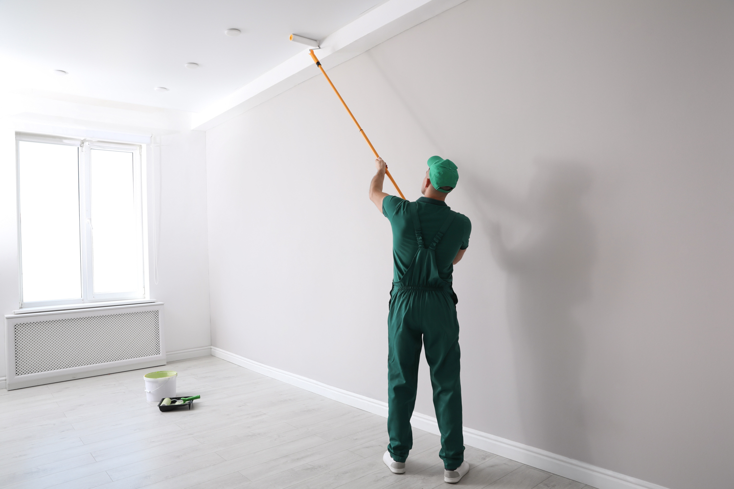 Man painting ceiling with roller in room back view